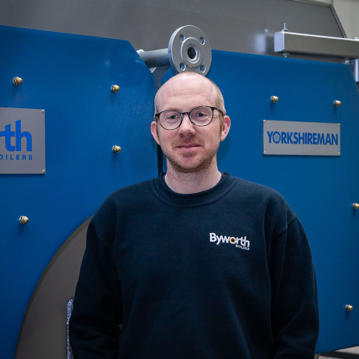 Man with bald head stood in front if an industrial boiler with blue heat sheilds